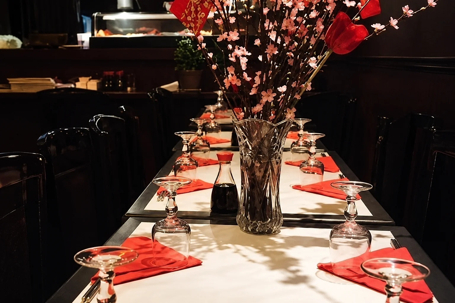 Table dressée avec verres retournés, serviettes rouges, sauce soja et vase de branches fleuries.